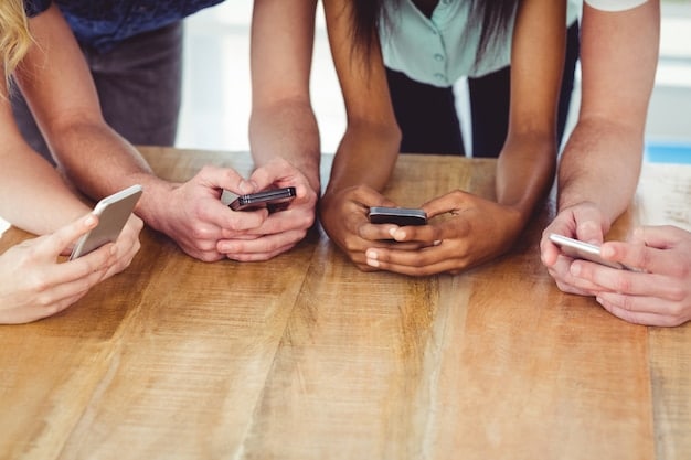 Close-up of a diverse group of hands holding and using smartphones, showcasing the variety of apps and activities they're engaged in, such as social media, gaming, and video conferencing.