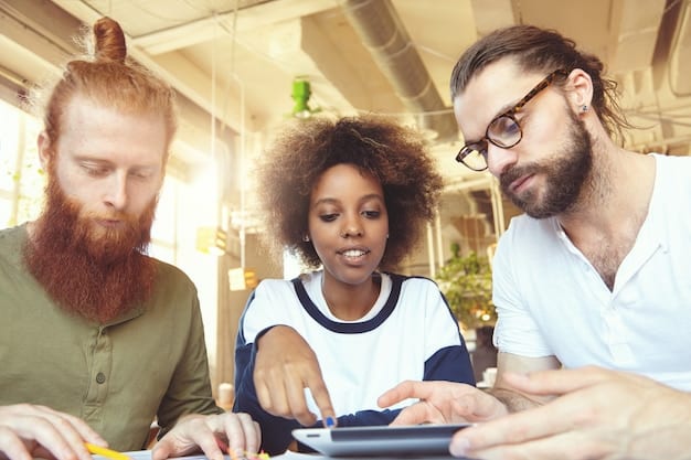 A group of diverse people interacting around a table, collaborating and using laptops and tablets. The scene reflects teamwork and social interaction.